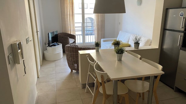 A modern kitchen with a dining table, chairs, a refrigerator, and a TV.