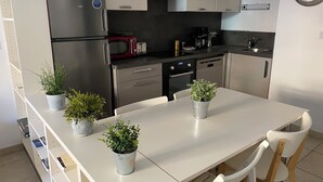 A modern kitchen with stainless steel appliances, a white dining table, and potted plants.