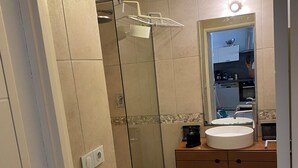 A modern bathroom with a glass-enclosed shower, a sink with a mirror above it, and a small rug on the floor.