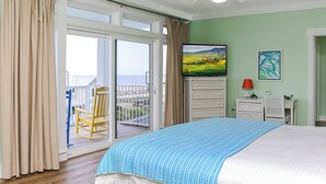 Ein Schlafzimmer mit einem großen Bett, einer Glastür zu einem Balkon, einem Deckenventilator und einem Gemälde an der Wand.