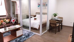Camera d'hotel moderna con un letto, una scrivania, una sedia, un divano, un divisorio in vetro e un tavolo da pranzo con una pianta.