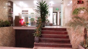 Una hall d'albergo con pavimento in marmo, una reception e una scalinata che conduce ai piani superiori.