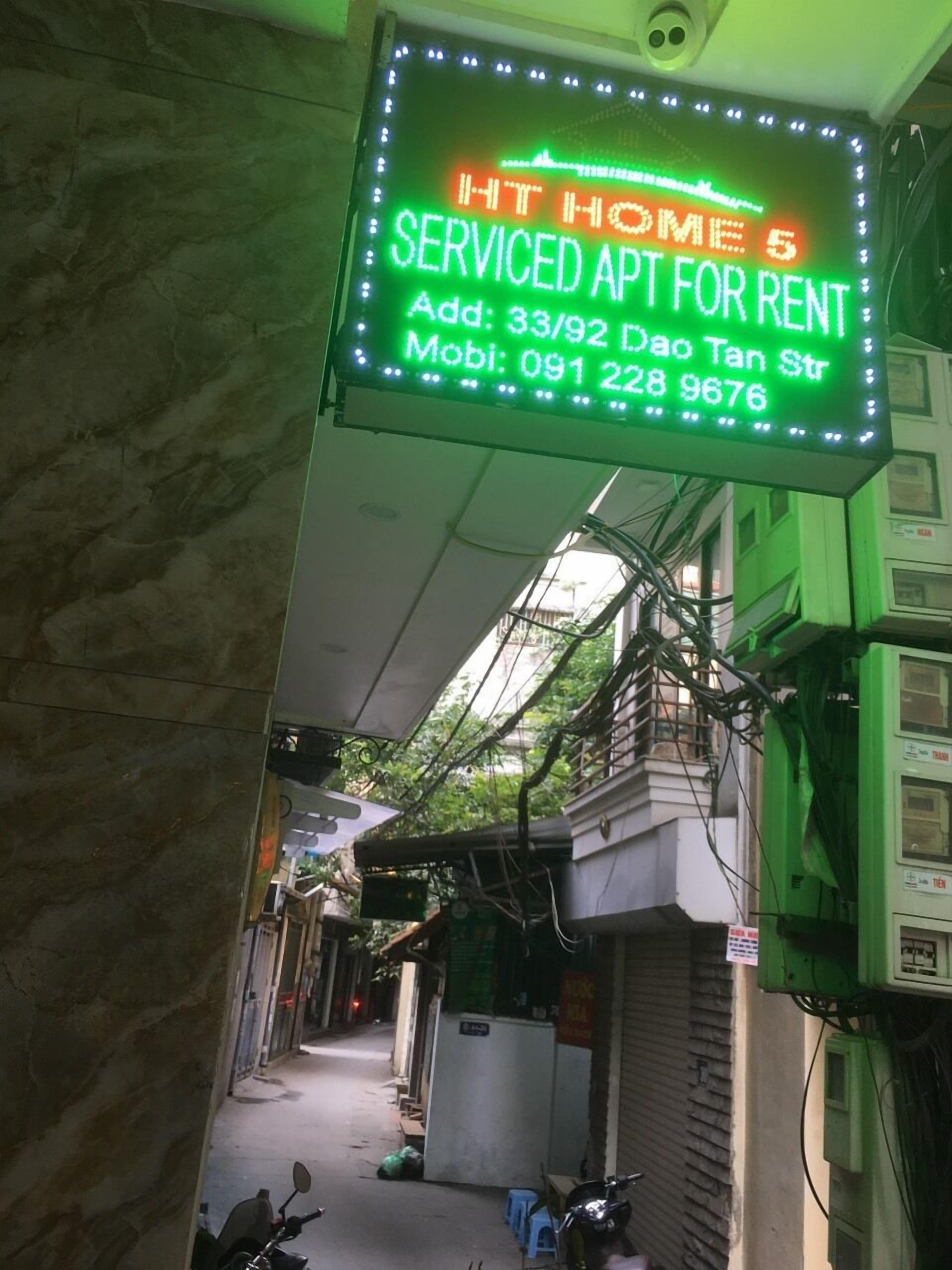 A neon sign advertising serviced apartments for rent at HT HOME 5, including an address and a mobile number.