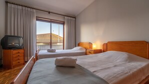 Una habitación de hotel con dos camas, televisión y ventana con vistas a edificios.