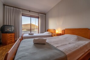 A hotel room with two beds, a television, and a window with a view of buildings.