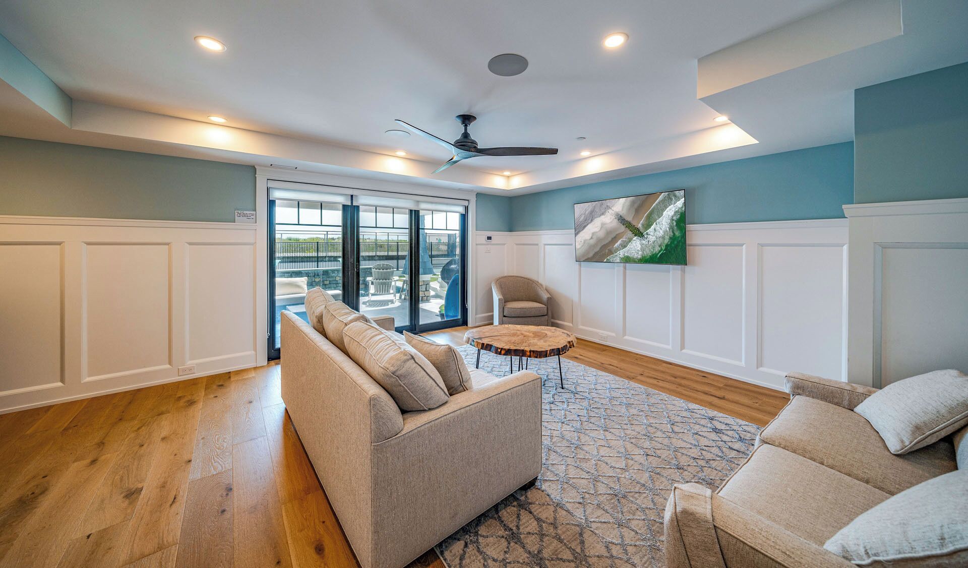A spacious living room with a large sofa, a smaller armchair, a coffee table, and a ceiling fan.
