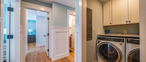 A laundry room with a front-loading washer and dryer, wooden flooring, and white cabinetry.