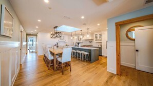 Une cuisine moderne avec un plancher en bois, des meubles blancs et un îlot central doté de tabourets de bar.