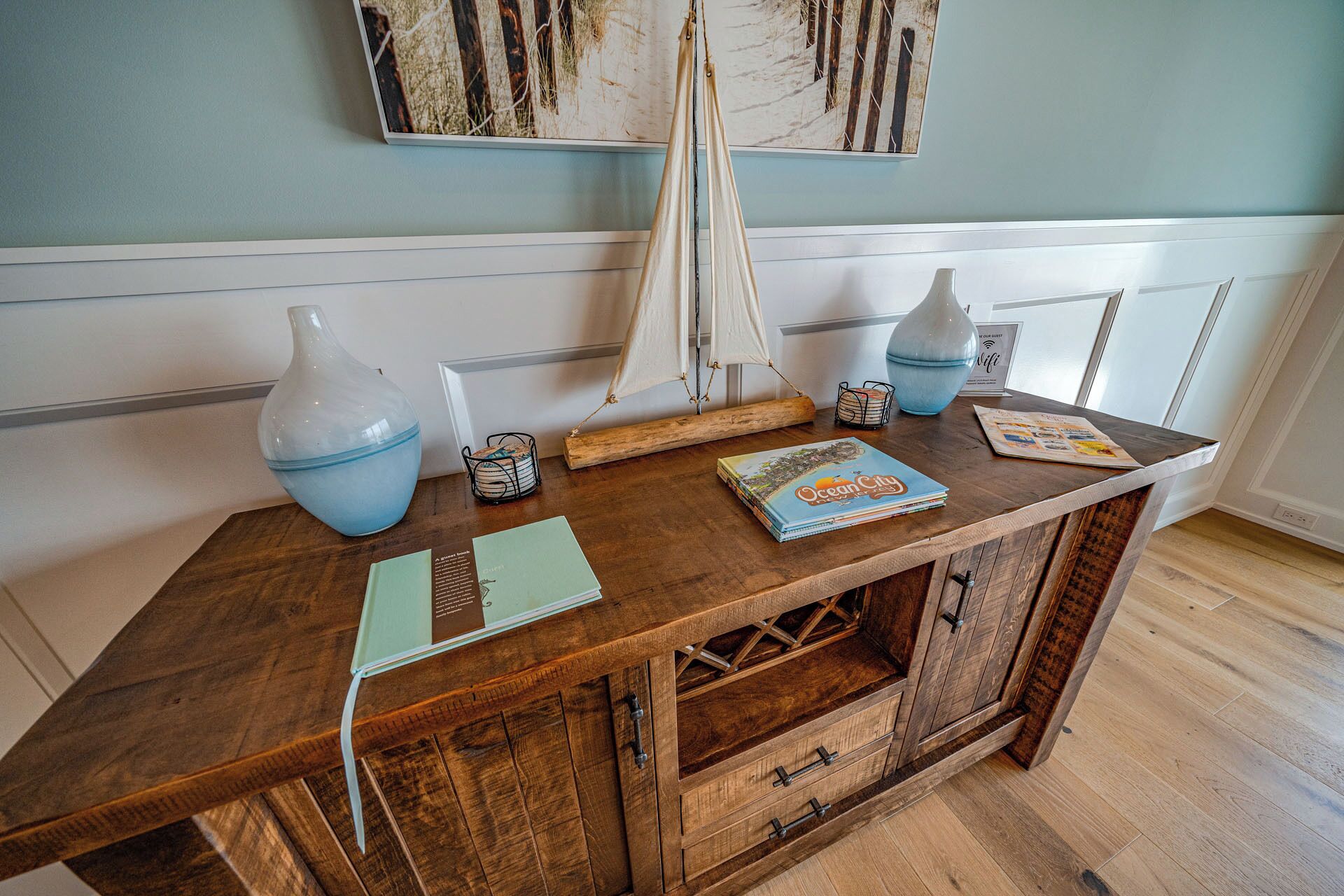 A wooden desk with a book titled "Ocean City," a vase, and a small table lamp.