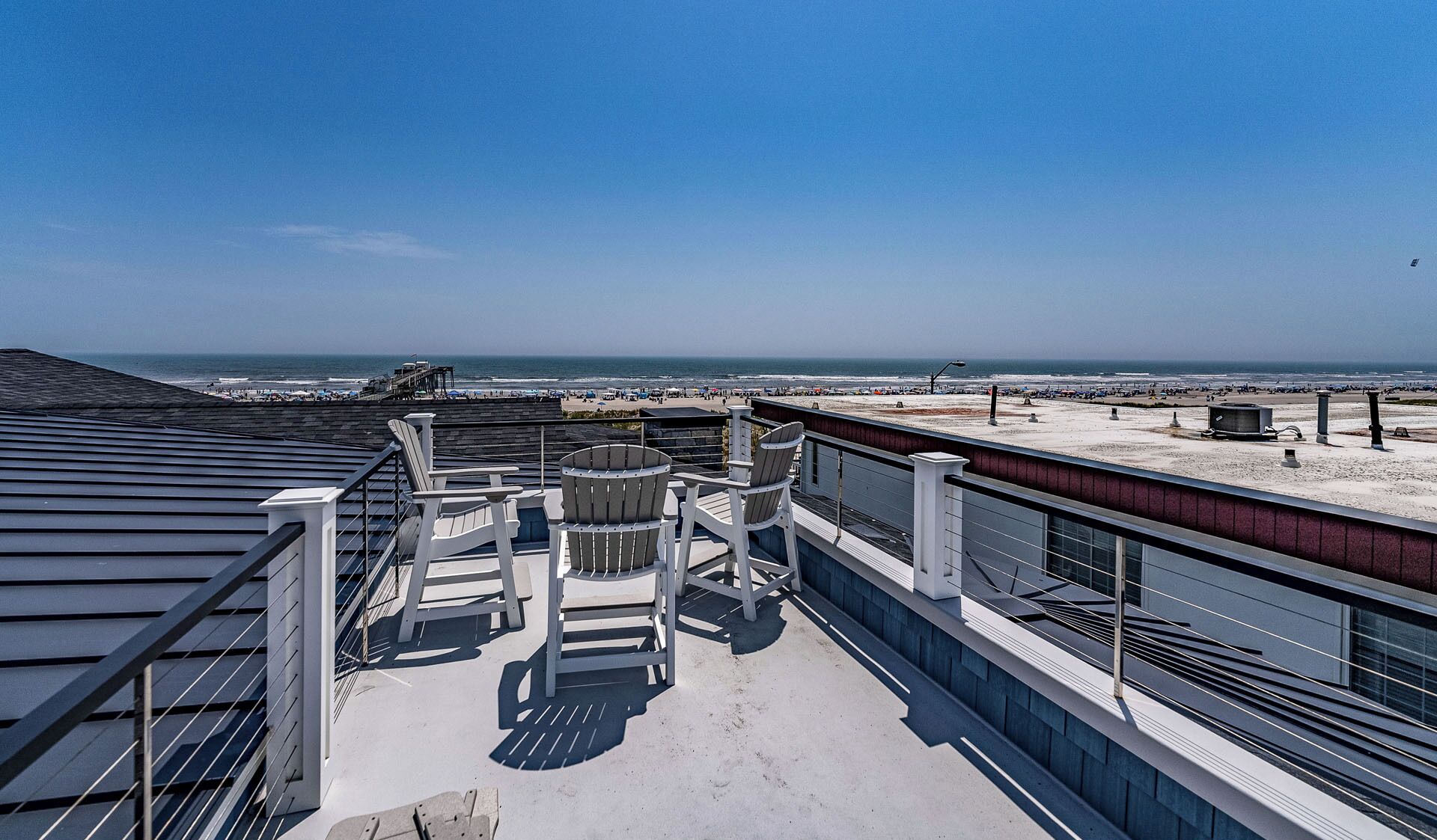 A rooftop terrace with a view of the beach, featuring outdoor seating and a railing.