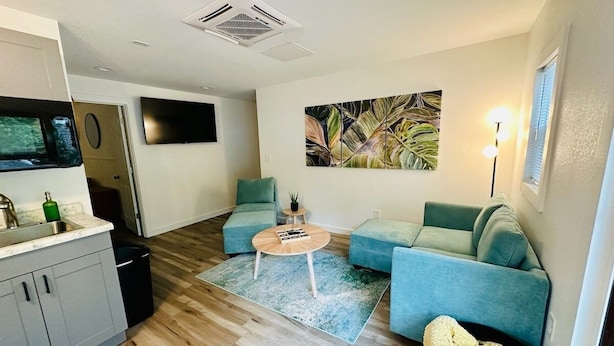 Uma sala de estar moderna com área de cozinha, apresentando um conjunto de sofás, uma mesa de centro e uma pintura na parede.