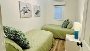 Quarto pequeno e acolhedor com duas camas, um ventilador de teto, obras de arte nas paredes e uma janela com persianas.