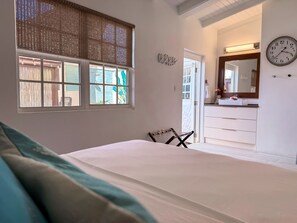 A bedroom with a bed, a window with blinds, a door leading to a bathroom, and a wall clock. - Kas di Almendra: Outdoor Shower, House Reef & Island Tours, By Ocean (Kralendijk)
