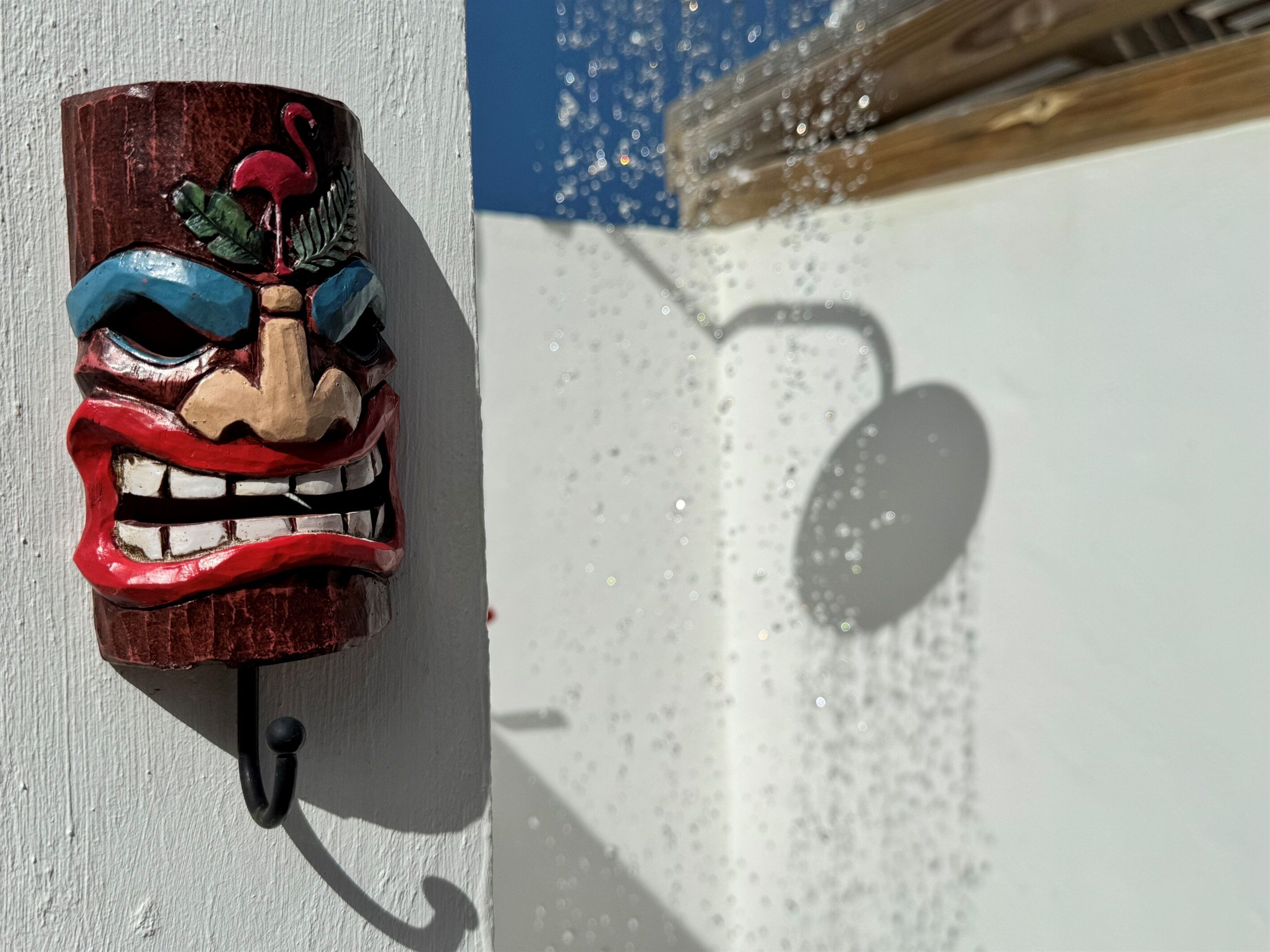 A wooden mask with a red mouth and blue eyes, mounted on a white wall.