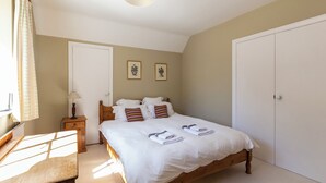 Ein Schlafzimmer mit einem hölzernen Bett, weißer Bettwäsche, einem Nachttisch mit Lampe und zwei gerahmten Bildern an der Wand.