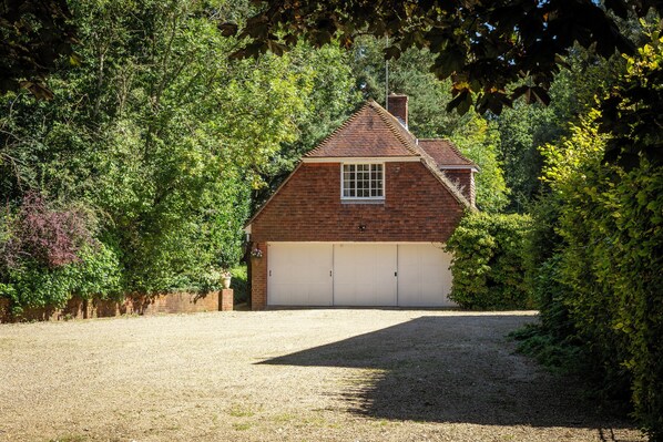 Een tweelaags bakstenen huis met een witte garagepoort, omgeven door weelderige begroeiing.