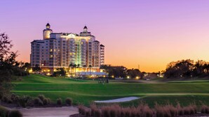 Ein großes Hotel mit mehreren Etagen und einem markanten Turm, umgeben von einem gepflegten Golfplatz.