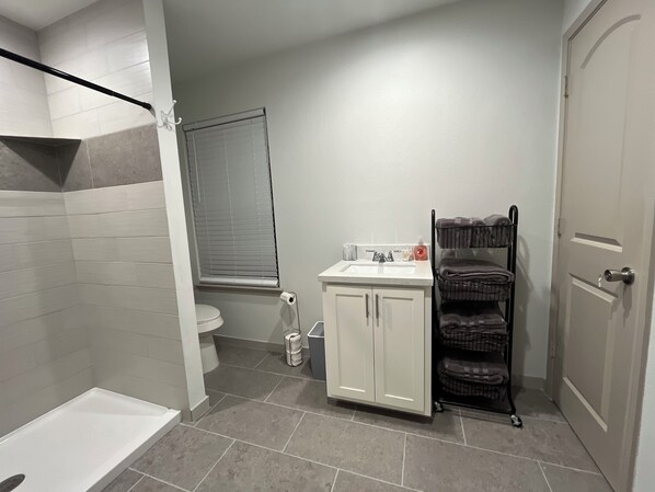 A bathroom with a shower, toilet, sink, and storage rack. - Magnolia Blooms: Spacious 5-BR 3.5 BA, tranquil, vibrant community. (Magnolia)