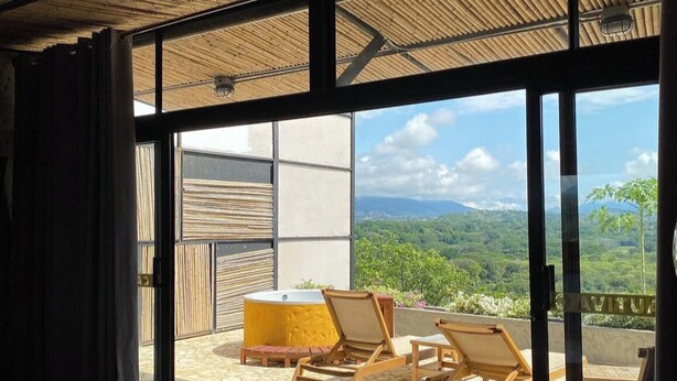 Ein Zimmer mit einer großen Schiebeglasdoor zum Außenbereich, der eine Holzterrasse mit gelbem Tisch und Holzstühlen bietet.