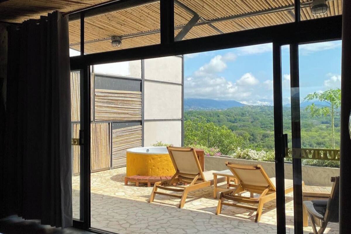A room with a large sliding glass door leading to an outdoor patio with wooden chairs and a yellow table.