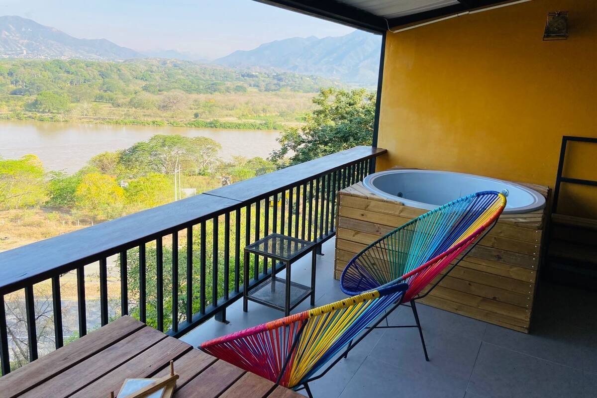 A balcony with a wooden table, colorful chairs, and a hot tub.