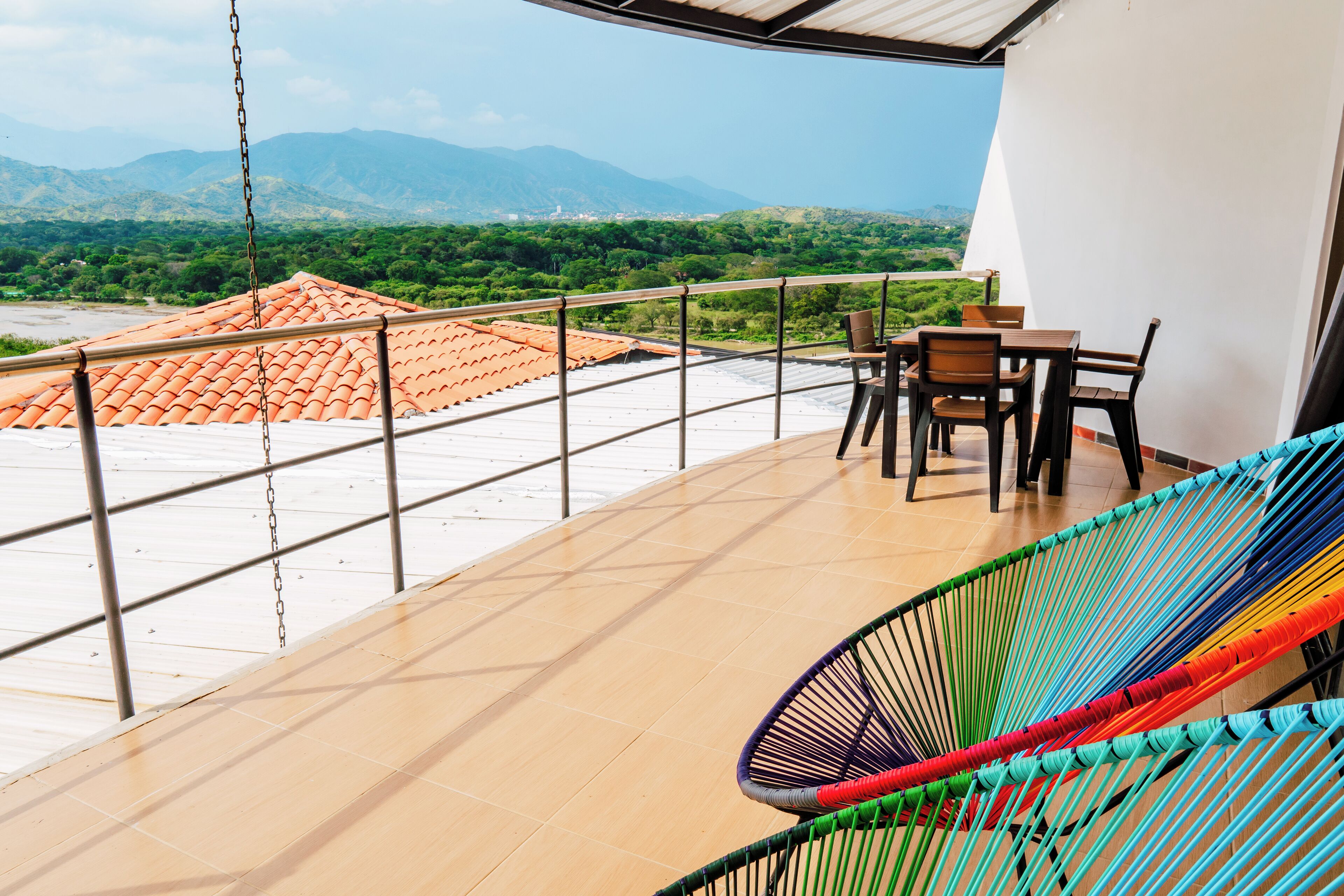 A balcony with a view of mountains, a table with chairs, and a colorful hammock.