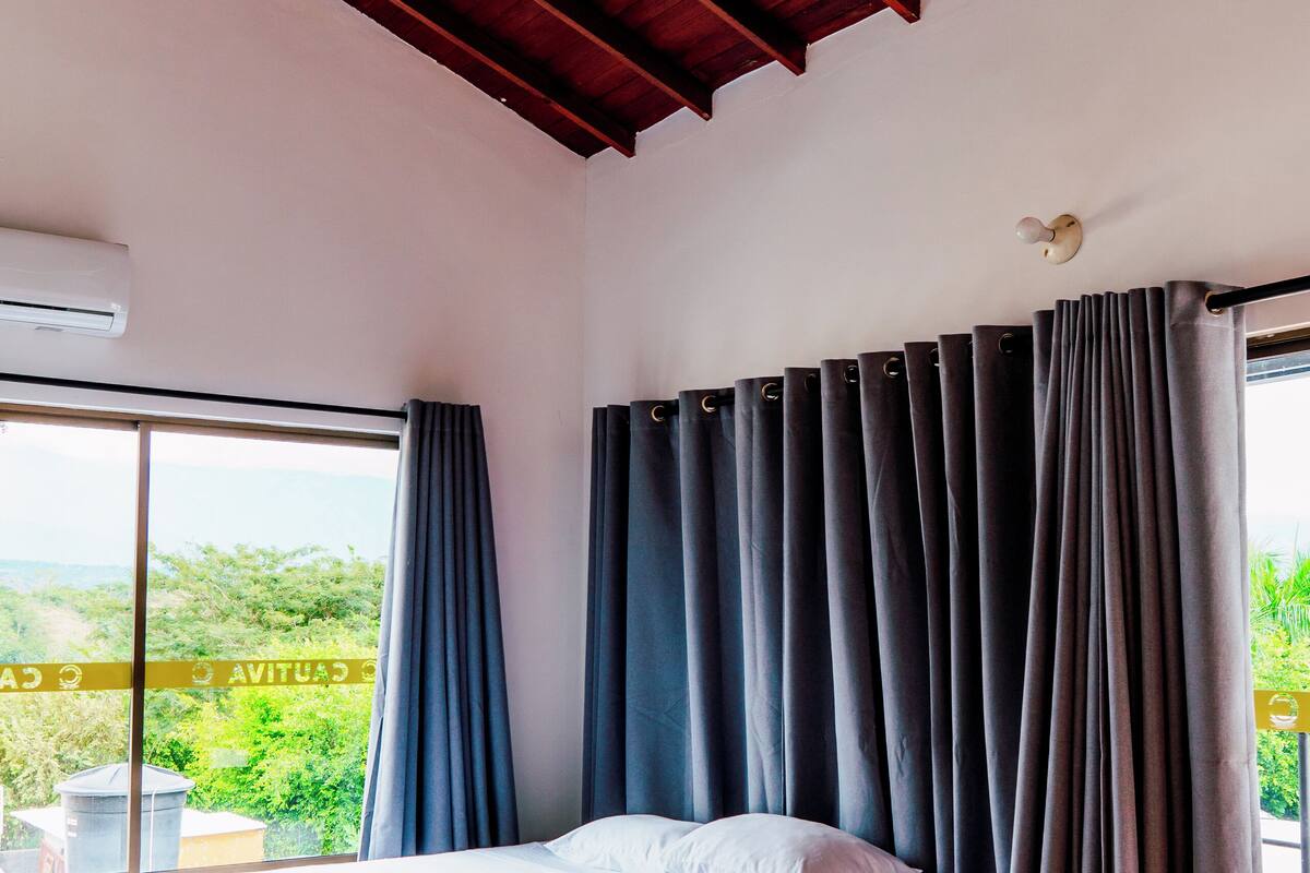 A bedroom with a large bed, a ceiling fan, and a view of greenery outside.
