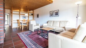 A modern living room with a wooden ceiling, white brick walls, and a red patterned rug.