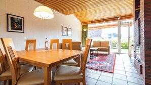 A dining area with a wooden table and chairs, a hanging light fixture, and a view of the outdoors through a glass door.