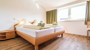 A bedroom with a wooden bed, a nightstand, a window with curtains, and a wooden floor.