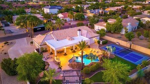 Una zona residenziale con una casa dotata di piscina, campo da tennis e portico coperto.