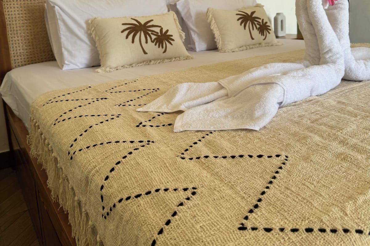 A neatly made bed with a woven headboard, white linens, and a decorative towel with a flower.