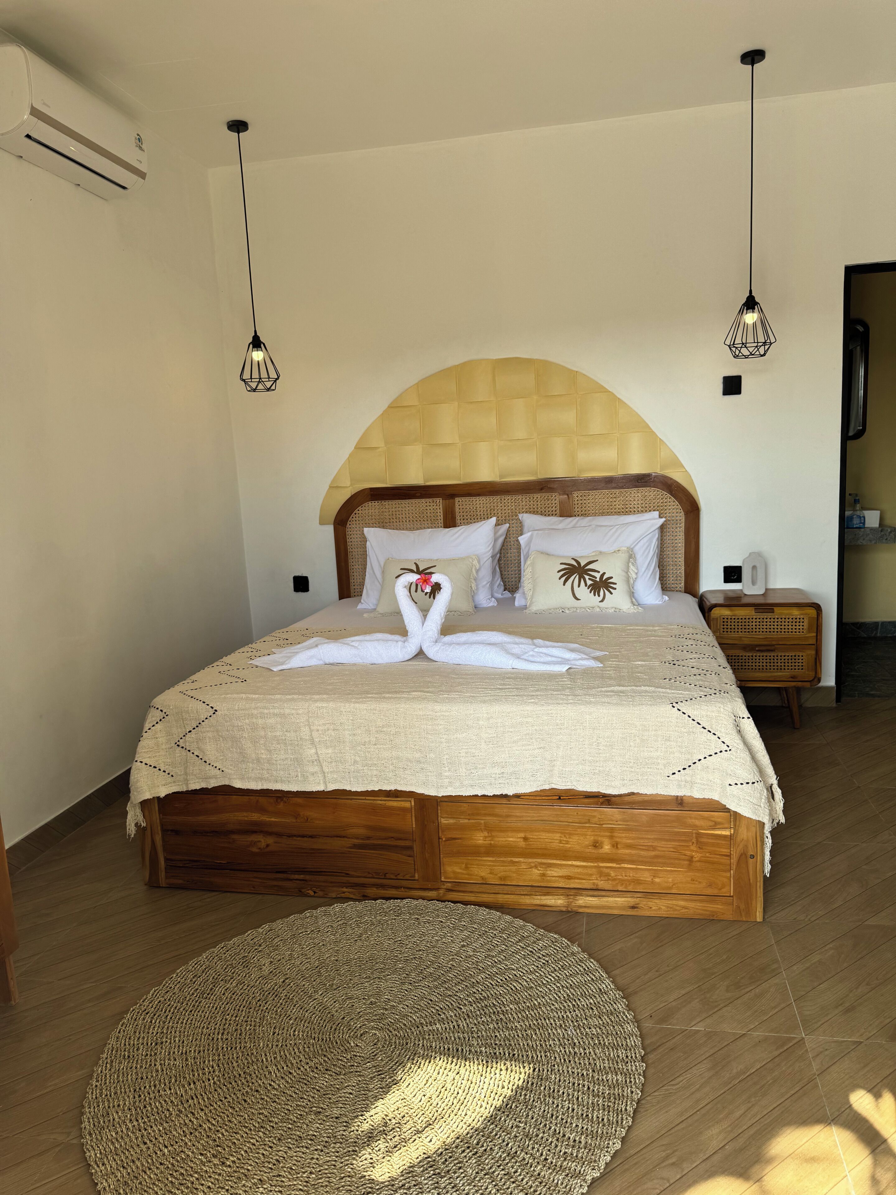 A neatly arranged bedroom with a large bed, two bedside tables, a woven headboard, and two pendant lights.