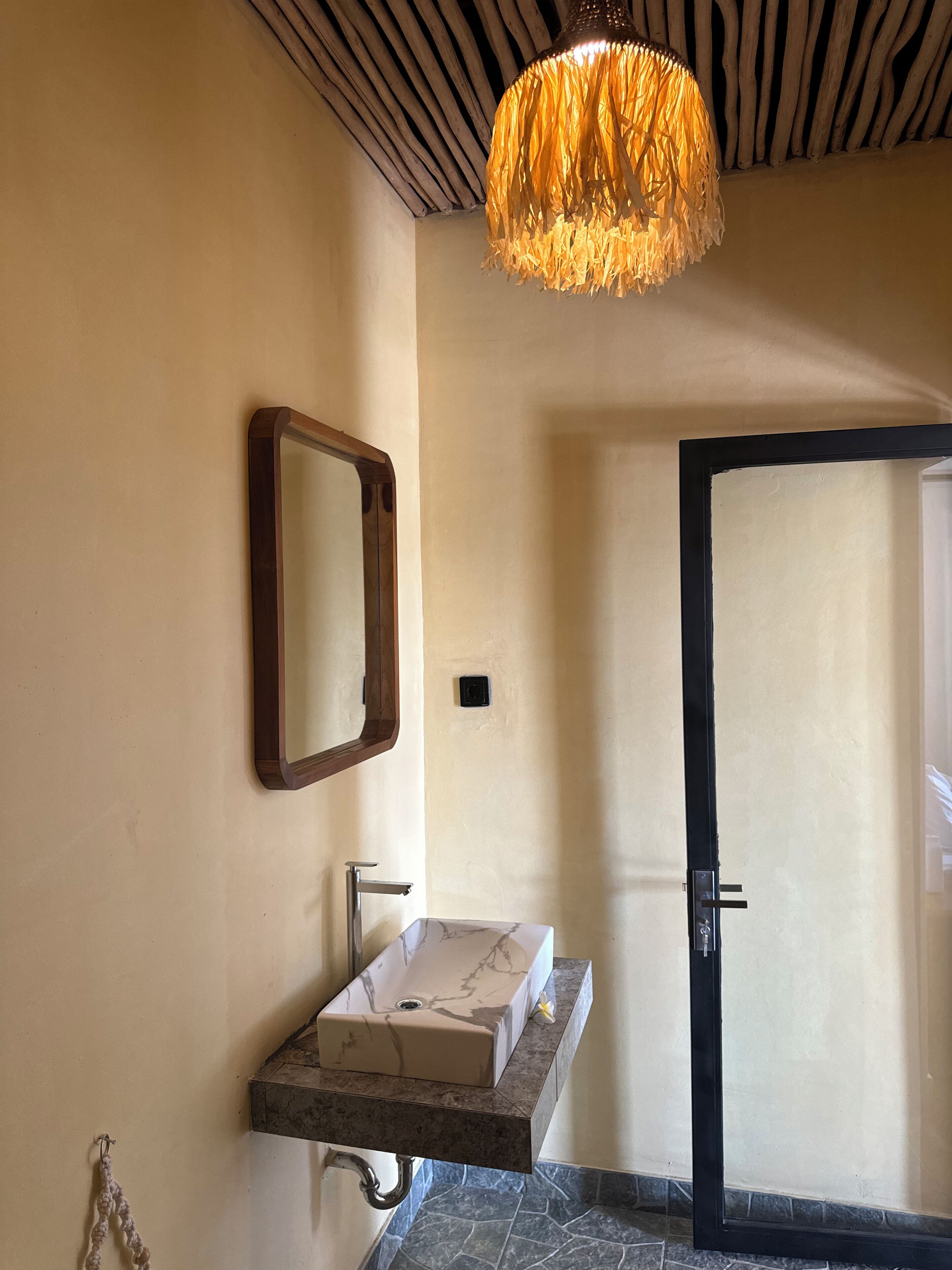 Un baño con lavamanos de mármol, espejo con marco de madera y una lámpara colgante original.