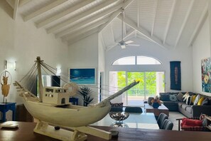 Uma sala de estar ampla com um modelo grande de barco, um ventilador de teto e vista para o exterior.