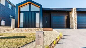 Stunning entrance to a modern home with a large glass door and garage door, set amidst a beautifully manicured lawn.