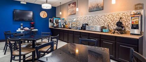 A restaurant with a blue wall, a counter with a coffee machine, and a TV mounted on the wall.