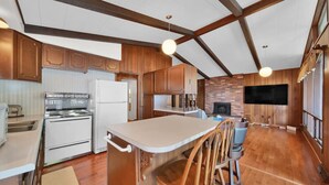 Una cocina con armarios de madera, un refrigerador blanco, una estufa y un comedor con un taburete y sillas.