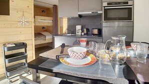 Une cuisine compacte équipée d’un four à micro-ondes, d’une machine à café et d’un réfrigérateur. On y trouve une table à manger avec une carafe, des tasses et un saladier.