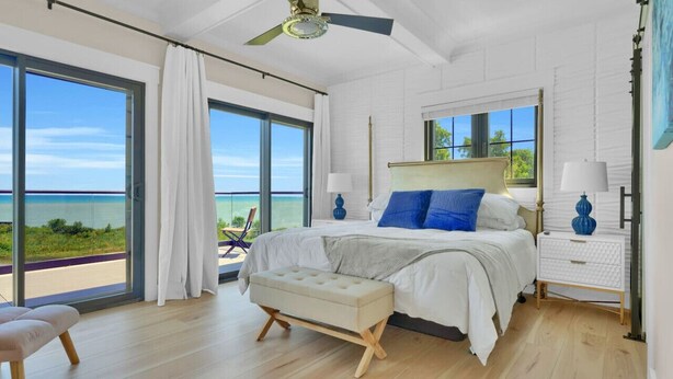 Une chambre à coucher avec un grand lit, un banc, une table de chevet et un ventilateur de plafond.