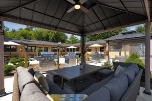 Un área de patio al aire libre con un espacio de estar techado, varias parrillas y vista a un edificio en el fondo.