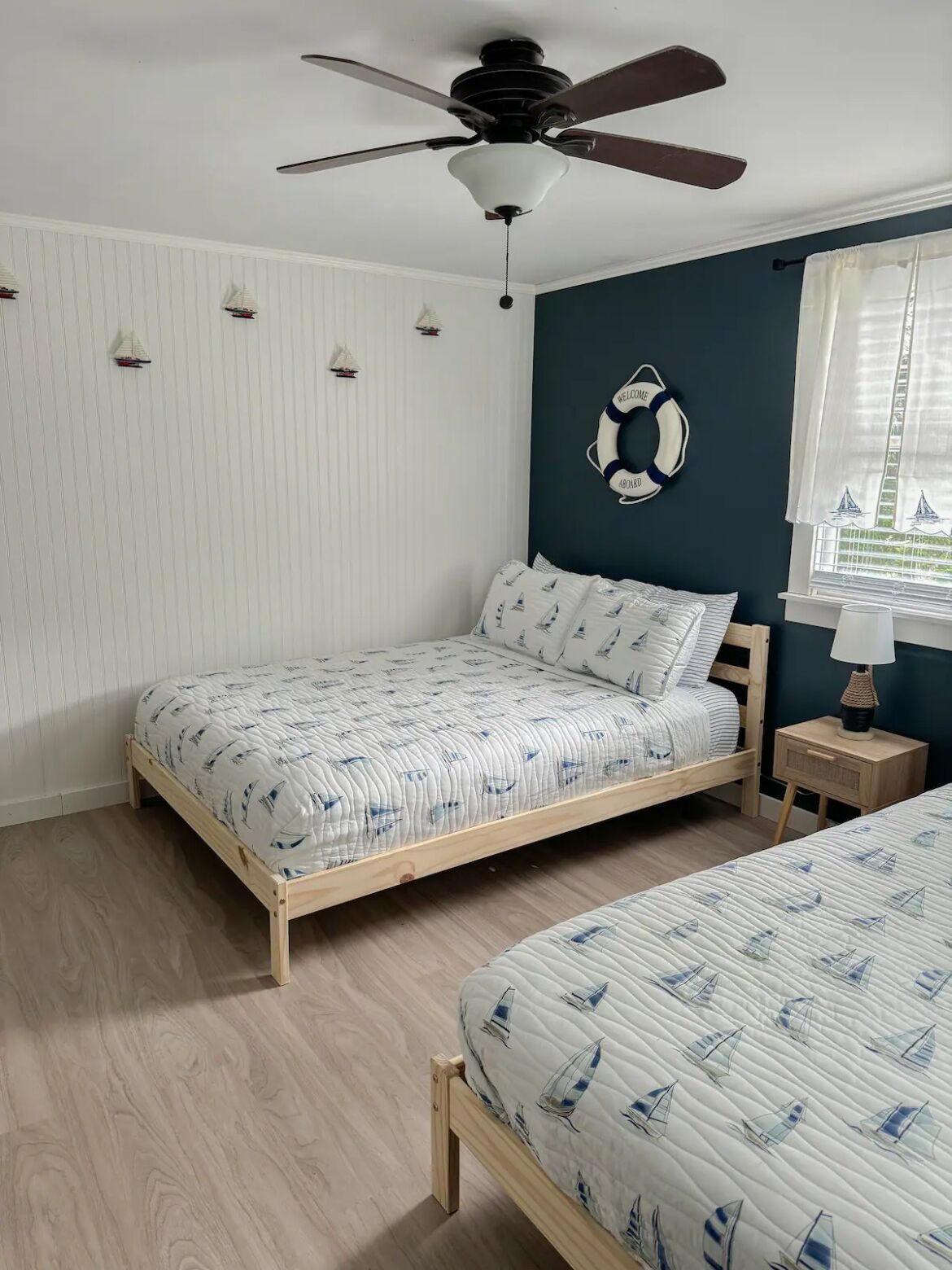 Une chambre à coucher avec un lit, un ventilateur de plafond, une table de chevet et une fenêtre avec des rideaux.
