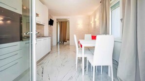 Una cocina moderna con armarios blancos y piso de mármol, que da a un área de comedor con sillas y mesa blancos.