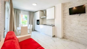 Una sala moderna con un sofá rojo, un comedor con mesa y sillas, y una cocina con armarios blancos y un televisor de pantalla plana montado en la pared.