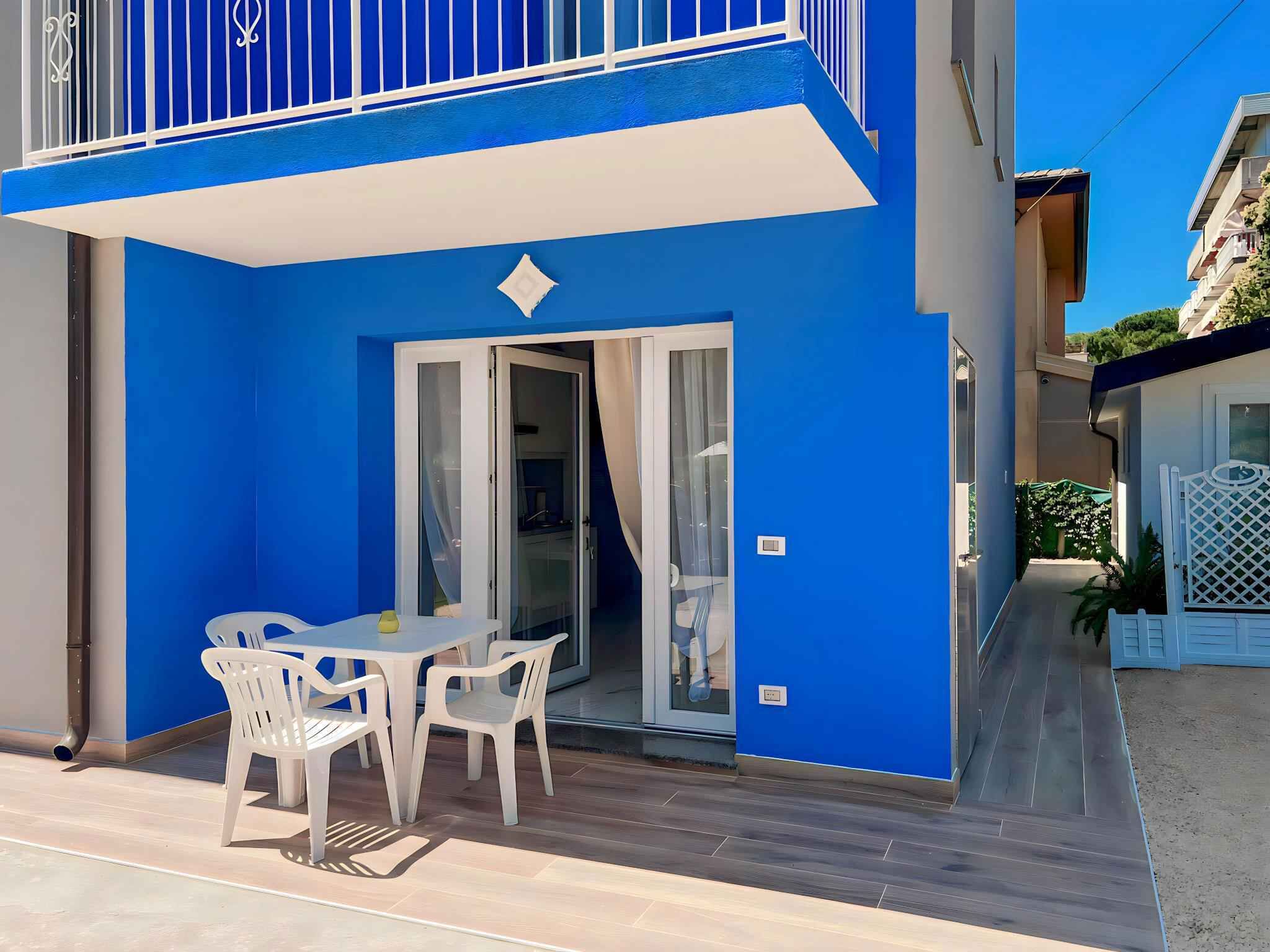 A blue building with a balcony, a sliding glass door, and a small patio with a table and chairs.