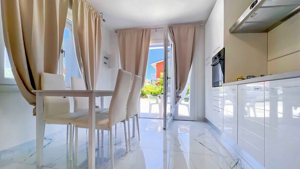 Una cocina moderna con gabinetes blancos, una campana extractora de acero inoxidable y un comedor con mesa y sillas.