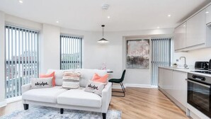 A modern living room with a white sofa, a green chair, and a kitchen area with a stove and cabinets. - Luxury 1 Bed Apt With City Views Heart of Leeds (Leeds)