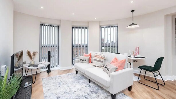 A modern living room with a white sofa, a small round table, and a green chair. - Luxury 1 Bed Apt With City Views Heart of Leeds (Leeds)
