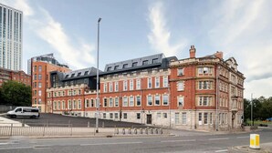 A historic building with a modern extension, featuring a mix of red brick and stone facades, large windows, and a flat roof. - Luxury 1 Bed Apt With City Views Heart of Leeds (Leeds)