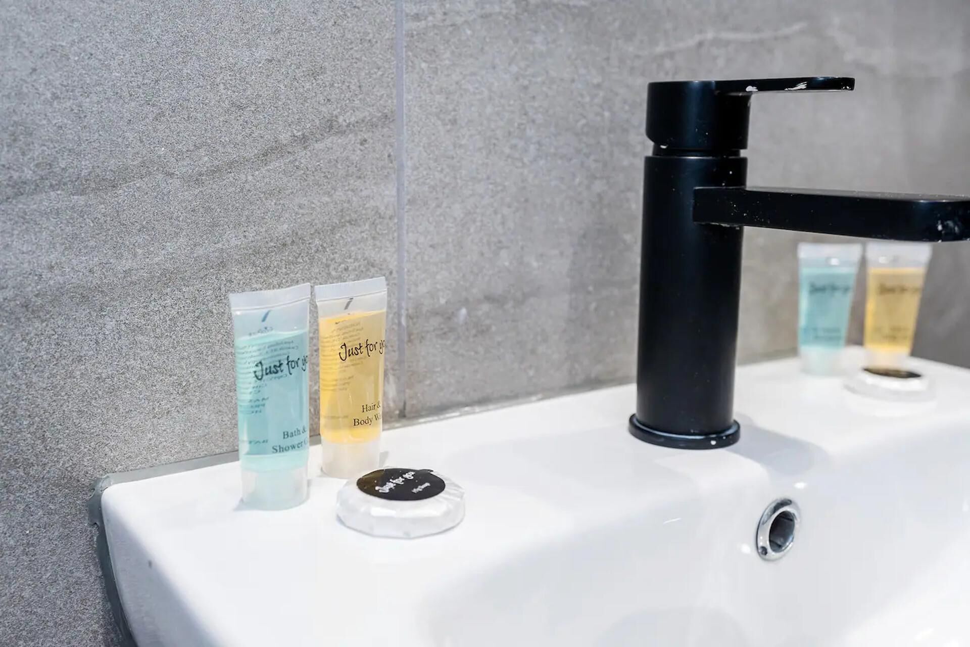 Un lavandino da bagno con un rubinetto nero e tre flaconi di shampoo e bagnoschiuma.